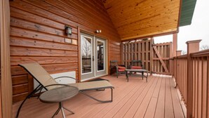 Una terraza de madera con techo, que cuenta con una puerta corrediza de vidrio, una mesa y dos sillones de descanso.