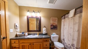 Un baño con muebles de madera, un lavamanos, un inodoro y una cortina de ducha.