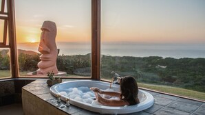 Una bañera con vistas al océano y una estatua Moai.