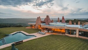 Una casa moderna con un diseño arquitectónico único que presenta estructuras prominentes similares a rocas. Incluye una piscina y un área de estar al aire libre.