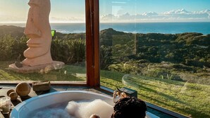 Una bañera con vistas a un paisaje exuberante y una gran escultura de piedra.