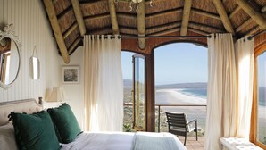 Une chambre avec un grand lit, un banc et une vue sur la plage.