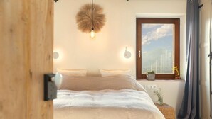 Un dormitorio con una cama grande, una lámpara colgante, una ventana con vistas y una puerta de madera.
