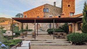 Un edificio de piedra con un patio cubierto, mesas al aire libre y una escalera de piedra que lleva a la entrada.