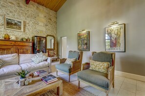 Una sala de estar acogedora con una pared de piedra, un sofá, dos sillones, una mesa de centro con libros y un cuadro enmarcado de Burdeos.