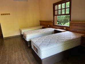 A room with two single beds, a window with a view of greenery, and a wooden headboard.