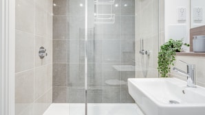 A modern bathroom with a glass-enclosed shower, a white sink, and a plant on the countertop. - Cozy London Apartment With 2 Bedrooms (London)