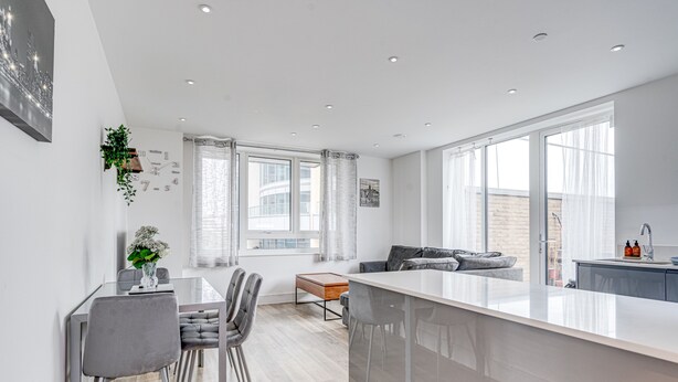 A modern kitchen with a central island, a dining area with chairs, a sofa, and a small table. - Cozy London Apartment With 2 Bedrooms (London)