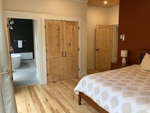 Un dormitorio con cama, armario de madera y baño visible a través de una puerta abierta.