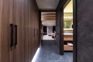 Un pasillo moderno que conduce a un dormitorio con una cama grande, una mesita de noche y un baño con lavabo y espejo.