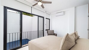 Ein Schlafzimmer mit Bett, einem Sessel, einem Deckenventilator und einem Balkon mit Geländer.