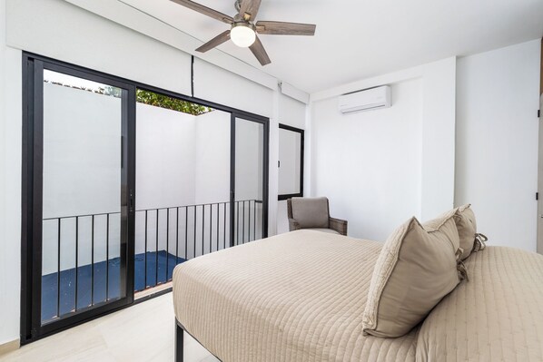 A bedroom with a bed, a chair, a ceiling fan, and a balcony with a railing.