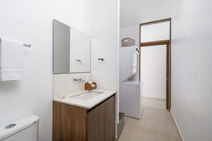 A modern bathroom with a wooden vanity, a large mirror, a toilet, and a washing machine.