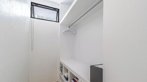 Ein schmaler Flur mit weißen Wänden, einem Fenster mit Metallrahmen und einem weißen Regal mit einem Handtuch und einem schwarzen Gegenstand.