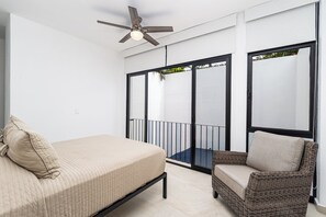 A bedroom with a bed, a chair, a ceiling fan, and a balcony with a view.