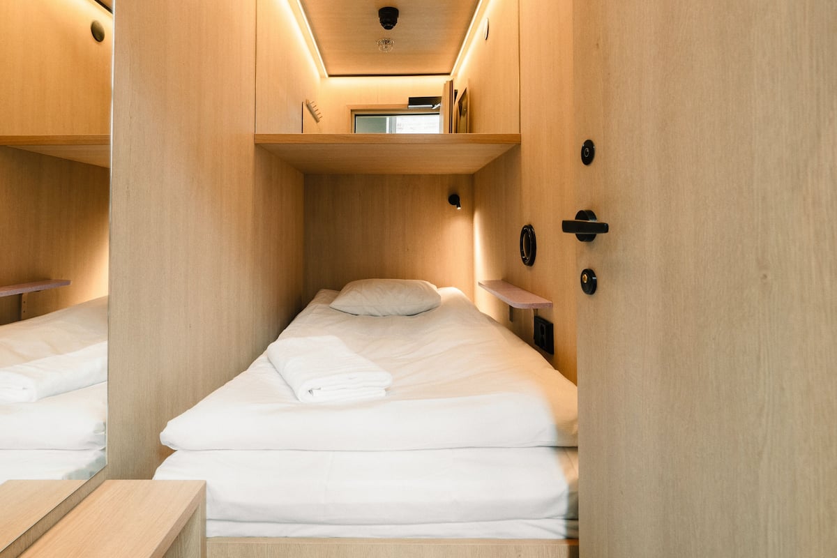 Une pièce compacte et bien éclairée, avec deux lits, des murs en bois et une petite étagère au-dessus des lits.