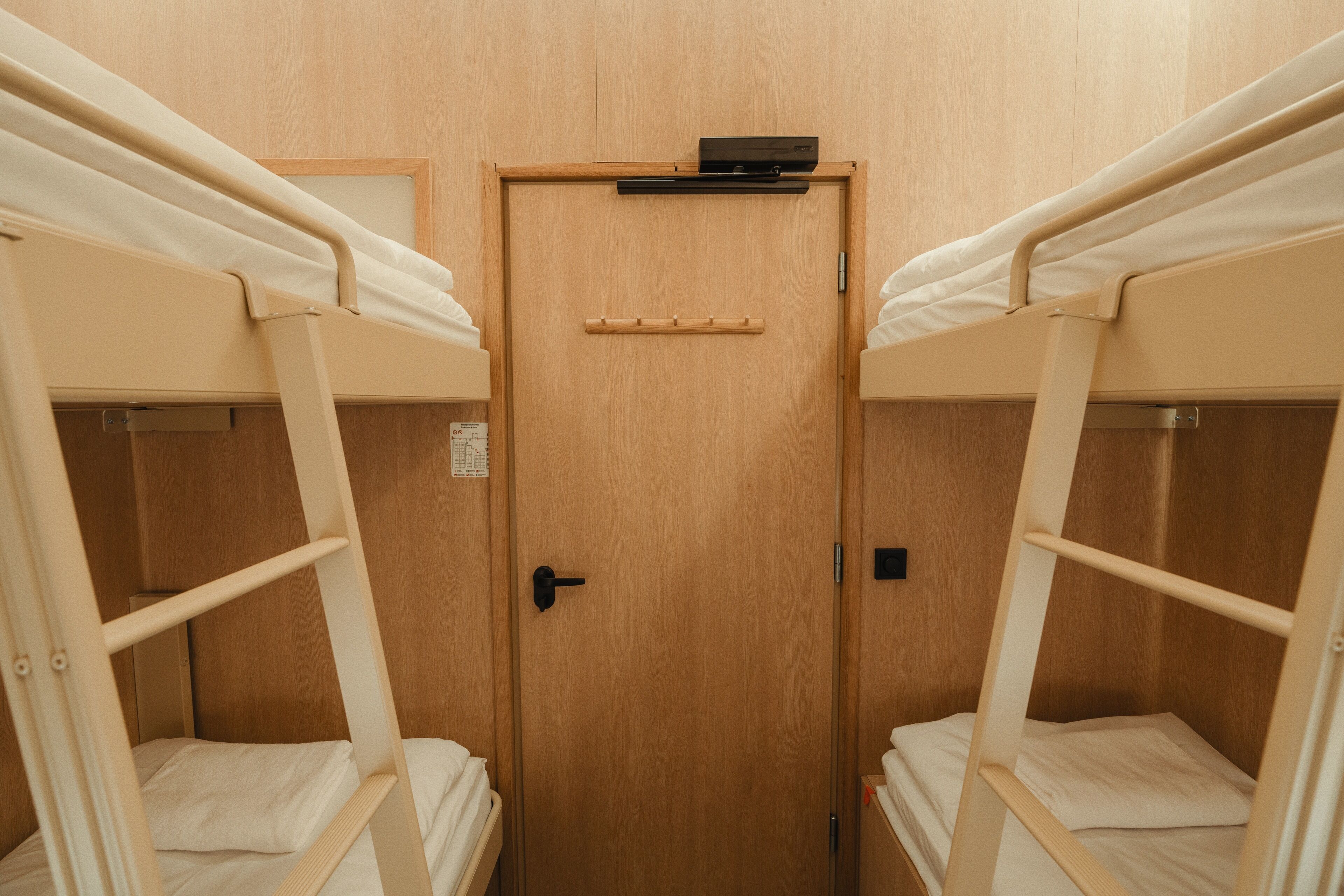 A room with two bunk beds, a wooden door, and a small shelf above the door.