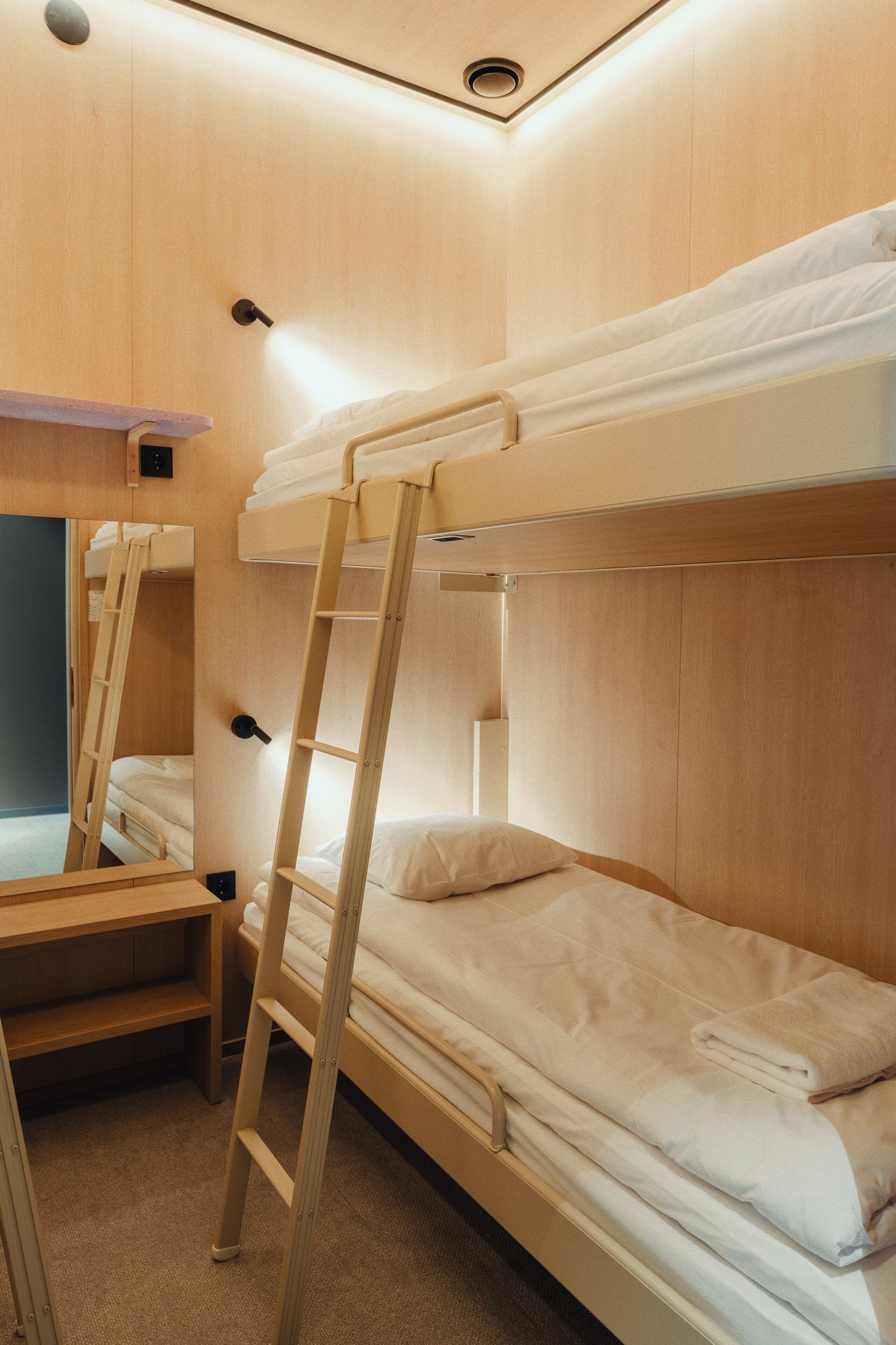 A bunk bed room with a wooden ladder and a small desk with a mirror.