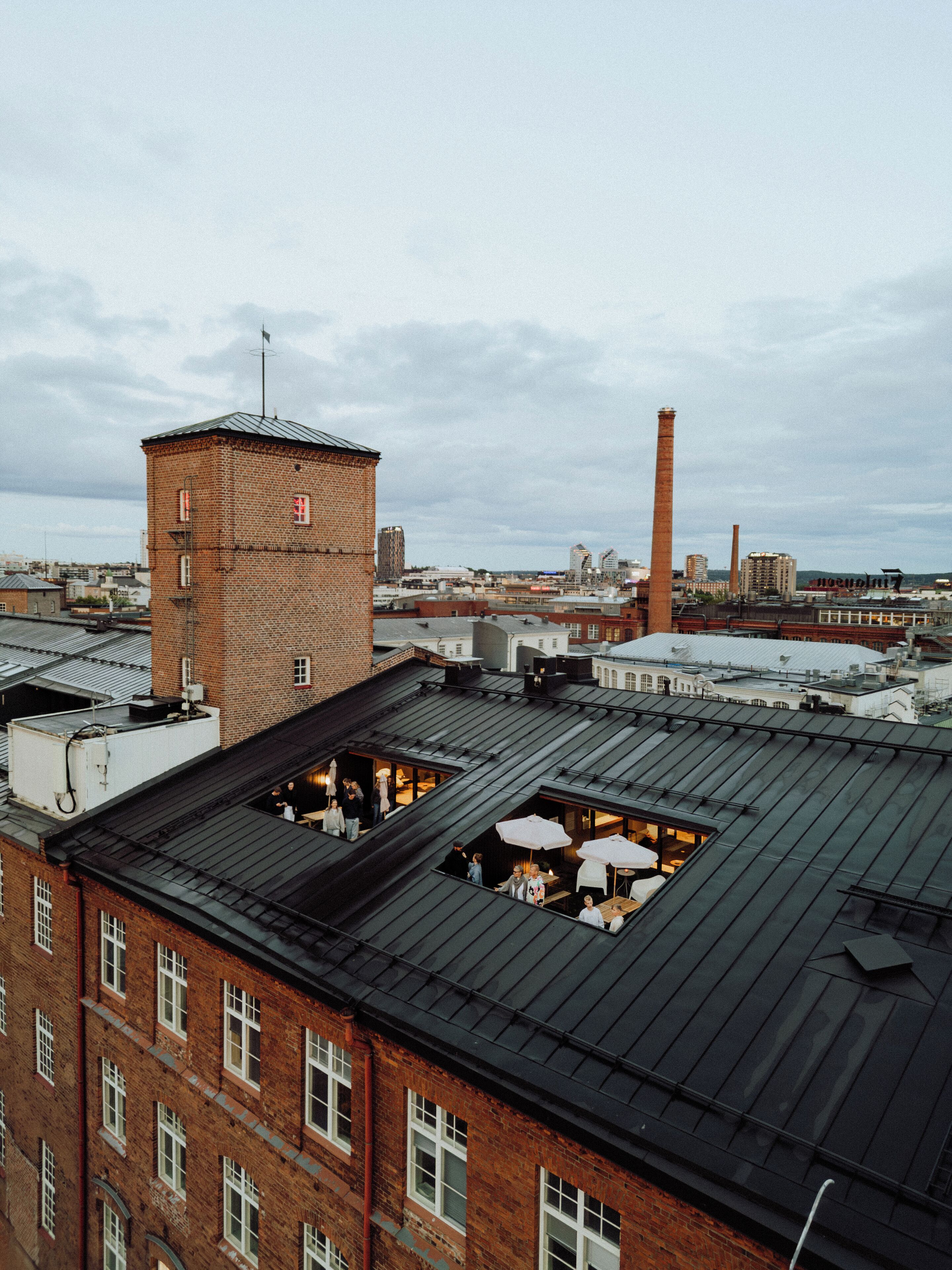 Una terrazza sul tetto con diversi tavoli e ombrelloni, circondata da edifici in mattoni e strutture industriali.