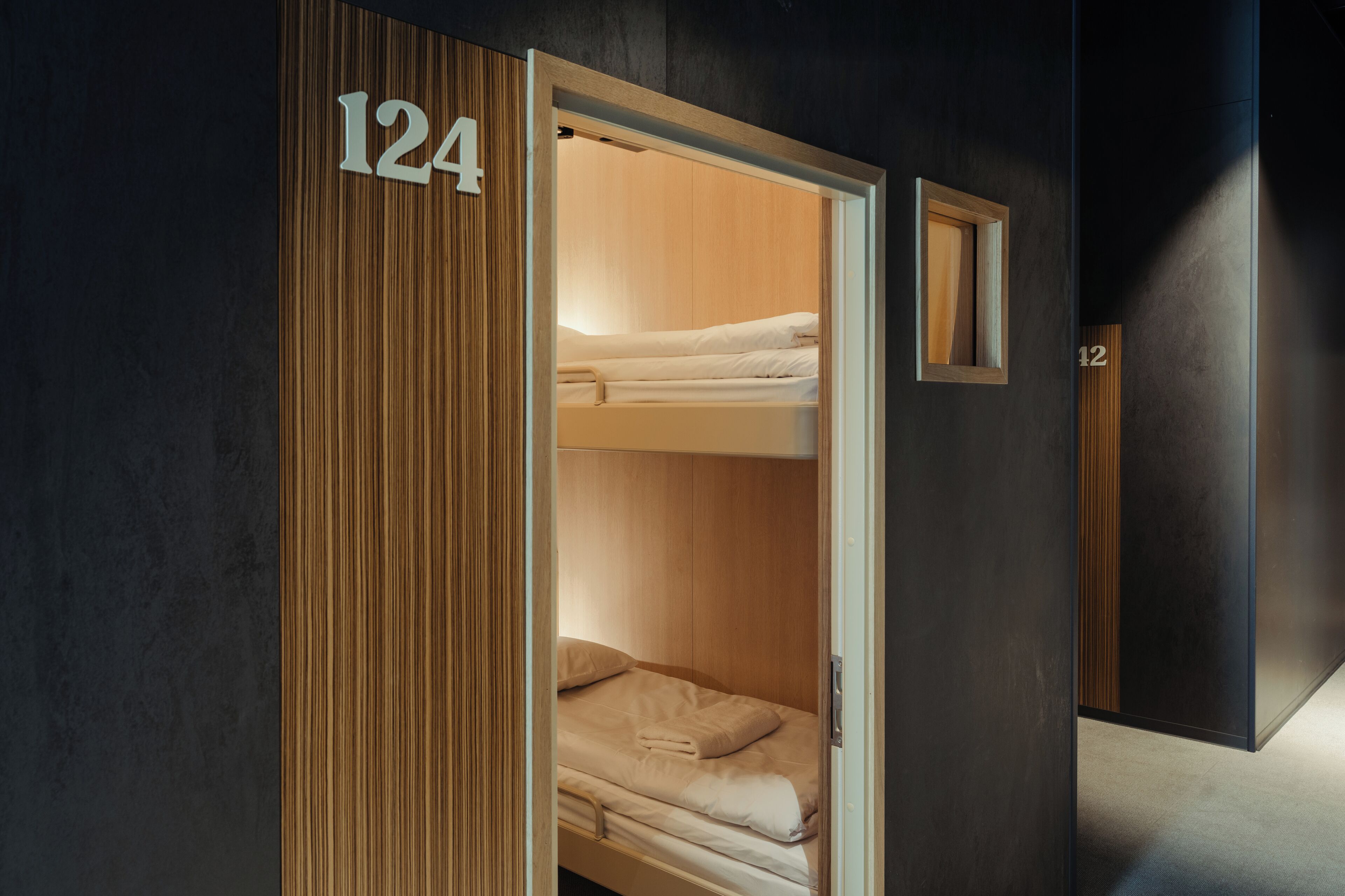 A room with a bunk bed, a wooden panel with the number 124, and a small window.