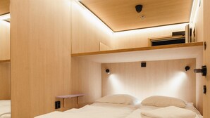 Ein kleiner, gut beleuchteter Raum mit einem Holzbett und einem kleinen Nachttisch.