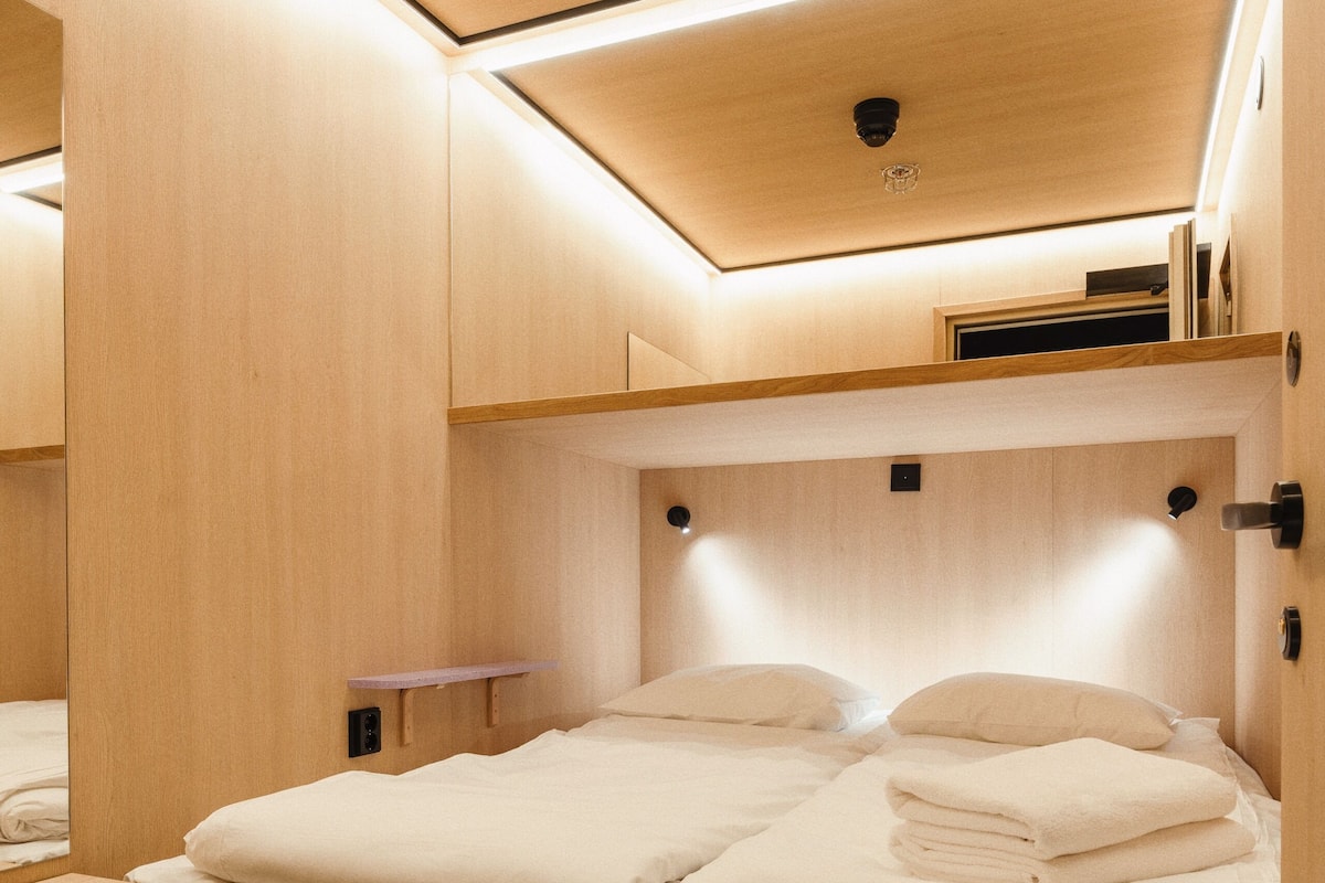 Une pièce compacte et bien éclairée, avec un lit superposé en bois et une petite table de chevet.