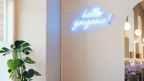Ein modernes Interieur mit einer Neonreklame, einer Topfpflanze und einem gestreiften Sessel.