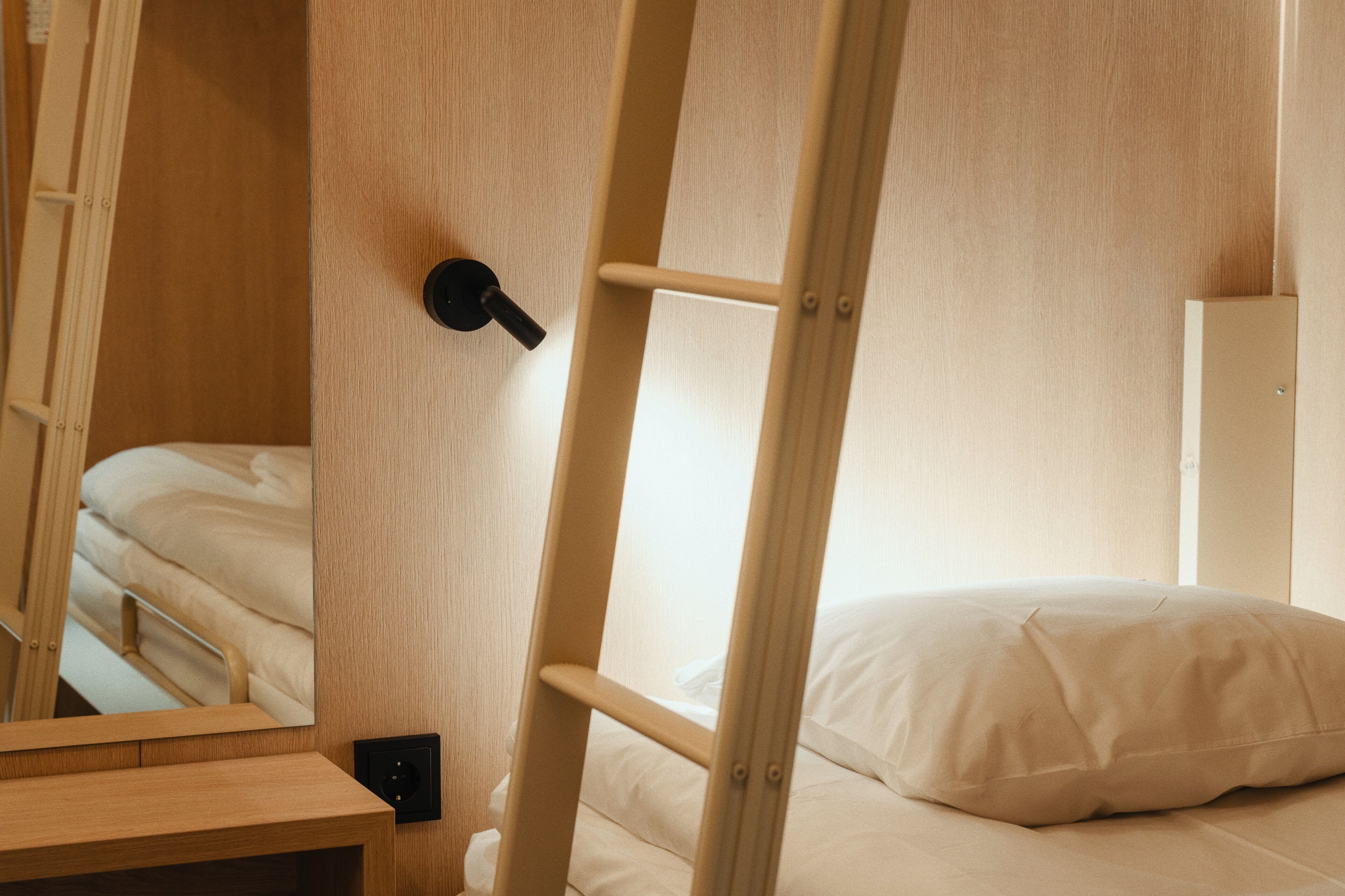 A bunk bed with a wooden ladder, a bedside table, and a wall-mounted light fixture.