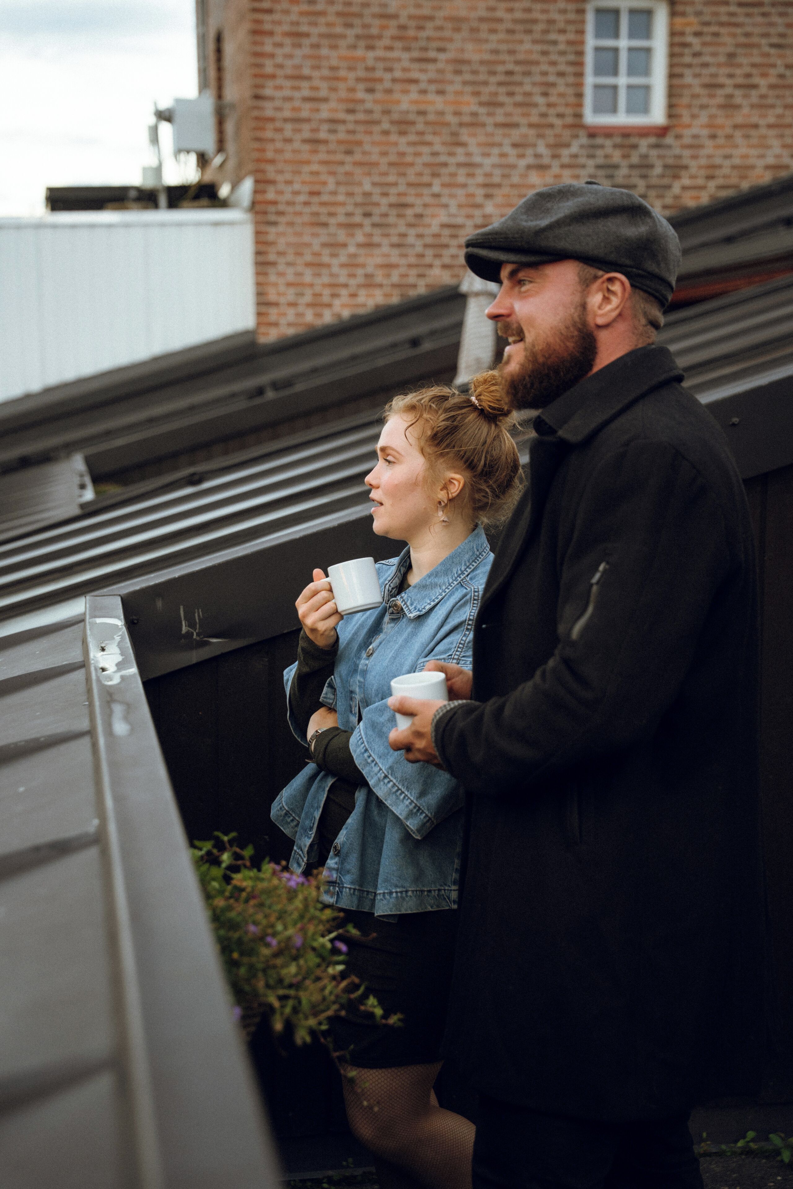 A man and a woman standing on a rooftop, holding white mugs.
