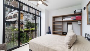 A bedroom with a bed, a large window, a ceiling fan, and a view of a courtyard with plants and a building. - DANNY HOUSE 2 (Puerto Vallarta)