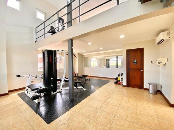 Un gimnasio espacioso con un entrepiso, diverso equipamiento de ejercicio y una amplia pared de espejos.