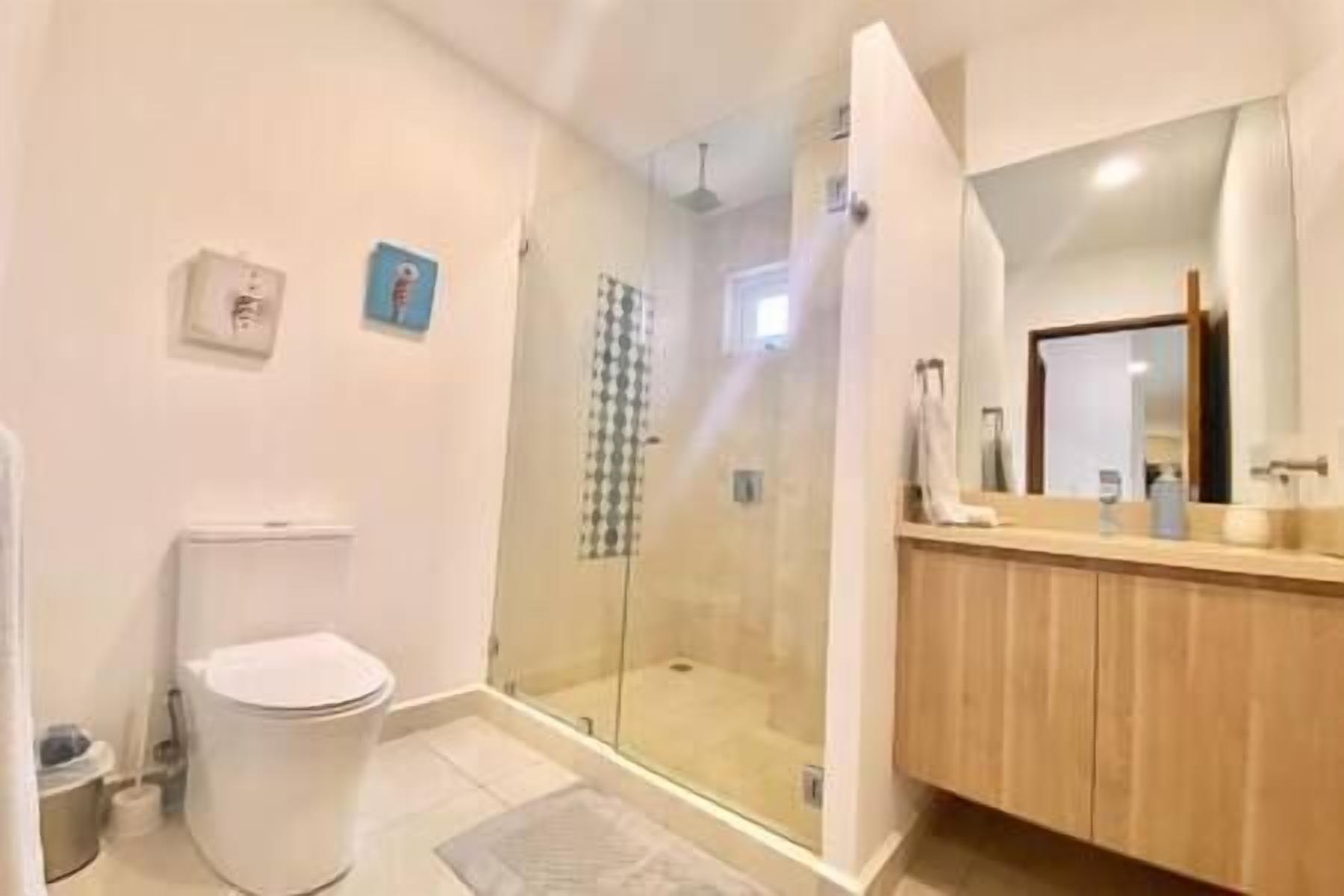 Un baño con inodoro, cabina de ducha de vidrio y tocador de madera con espejo.