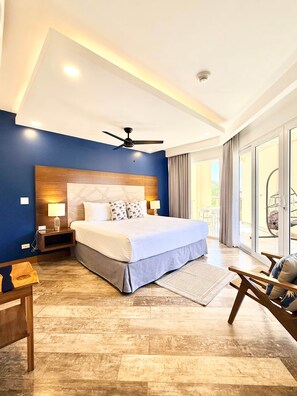 Une chambre d’hôtel moderne, dotée d’un grand lit, d’un ventilateur de plafond et offrant une vue sur l’extérieur grâce à une porte vitrée.