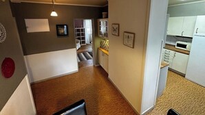 A narrow hallway leading to a kitchen with white cabinets and a microwave.