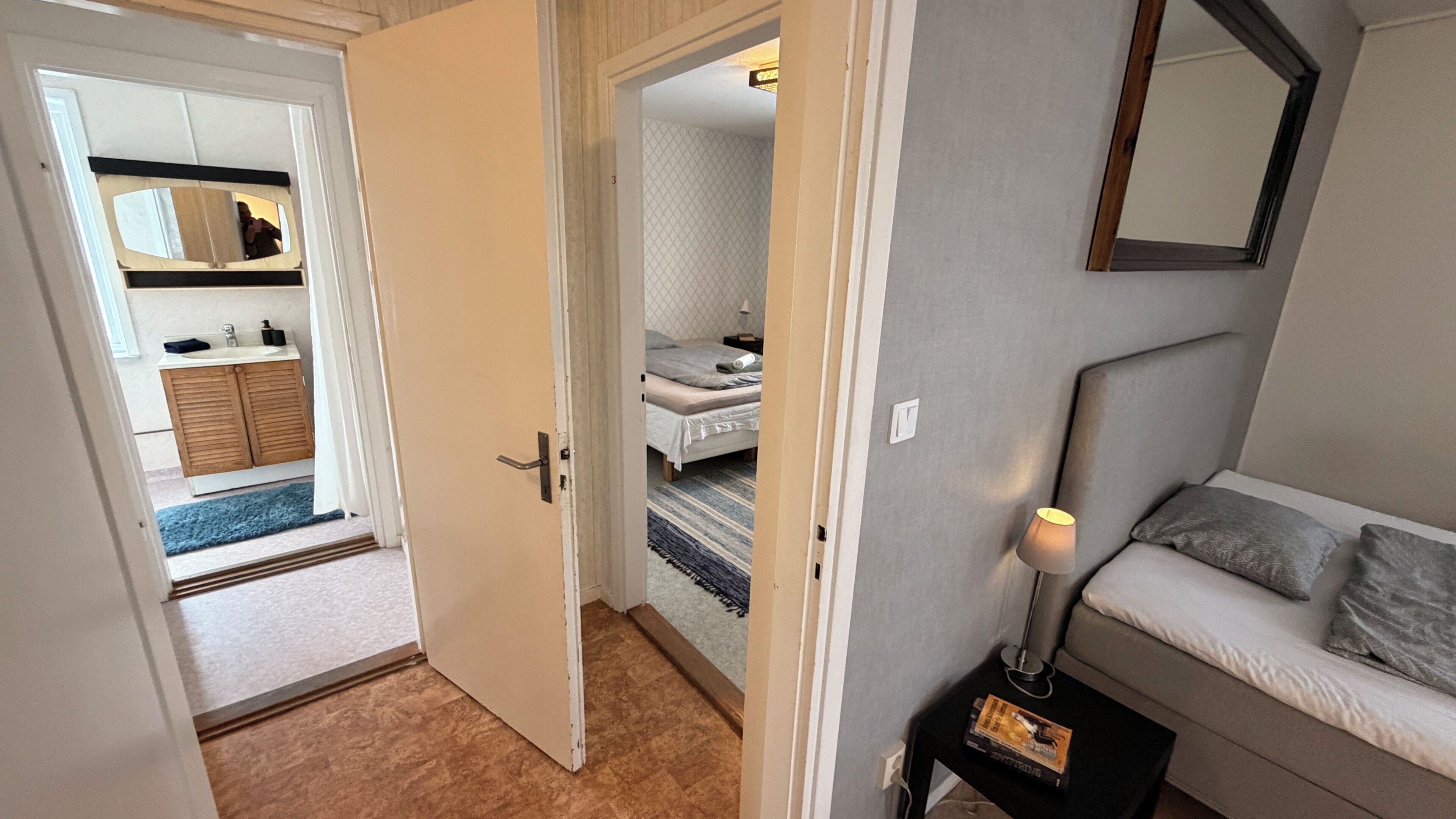 A room with a bed, a bedside table with a lamp, a sofa, and a mirror on the wall.