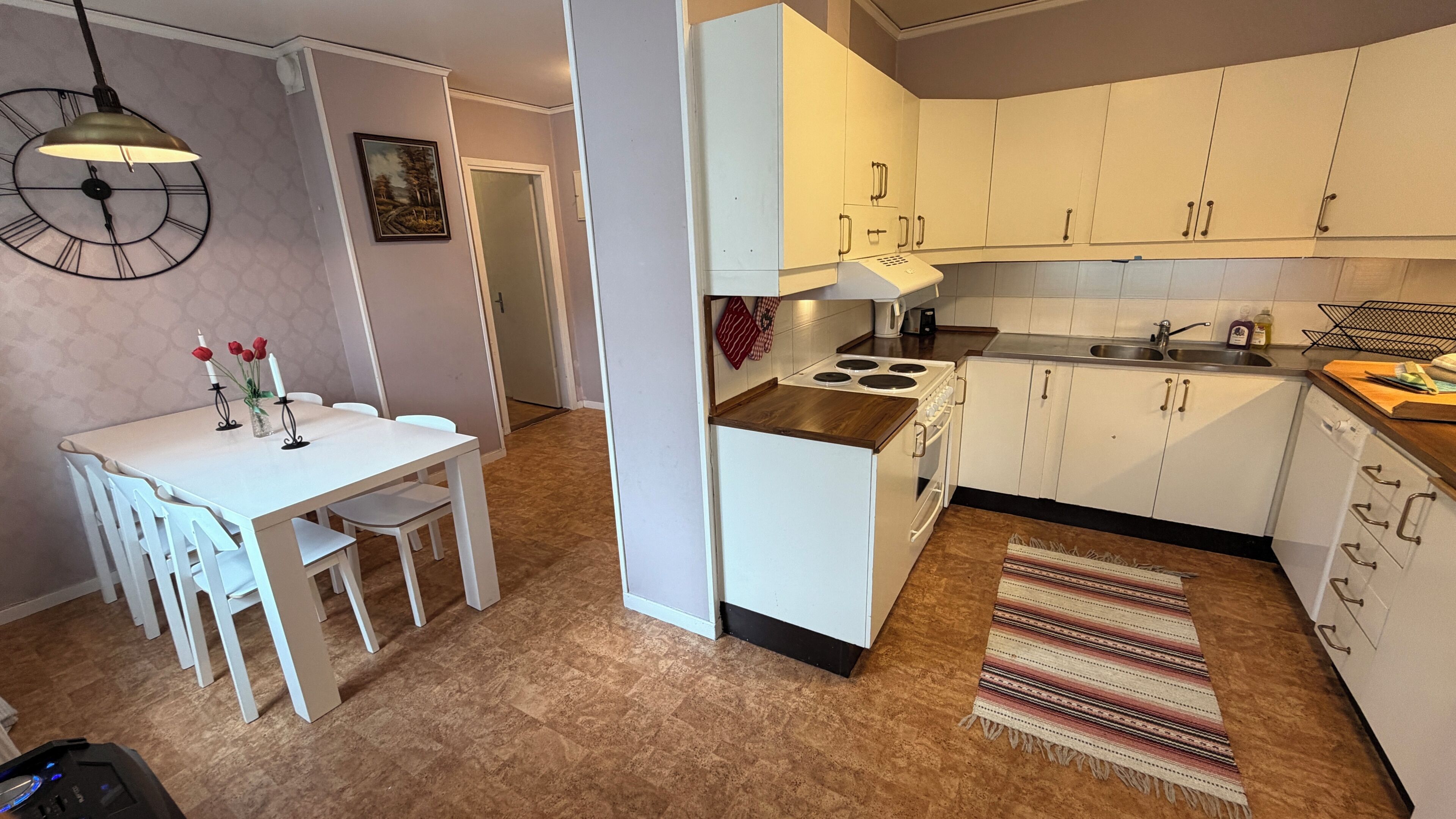 Une cuisine compacte avec des meubles blancs, une cuisinière et un coin repas comprenant une table et des chaises.