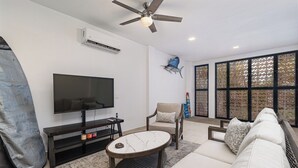 Un salon équipé d’un téléviseur à écran plat, d’un ventilateur de plafond, d’une grande fenêtre à croisillons et d’un canapé.