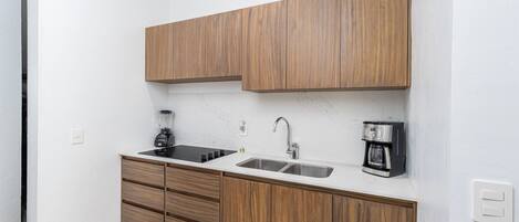A modern kitchen with wooden cabinets, a black induction cooktop, a stainless steel sink, and a coffee maker.