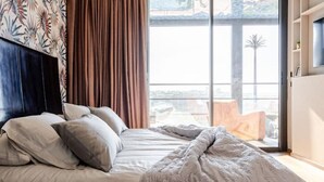 A bedroom with a bed, pillows, a blanket, a window with curtains, and a view of the outdoors. - Modern Ocean View Apartment - Pestana AnfaPlace (Casablanca)