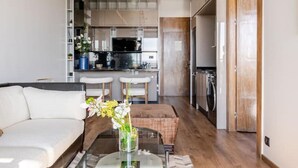 A modern living room with a sofa and a coffee table, a kitchen with a microwave, refrigerator, and sink, and a wooden door leading to another room. - Modern Ocean View Apartment - Pestana AnfaPlace (Casablanca)