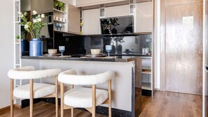 A modern kitchen with a central island, bar stools, and a TV. - Modern Ocean View Apartment - Pestana AnfaPlace (Casablanca)