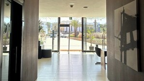A modern hallway with a view to an outdoor area, featuring a glass door, a ceiling with recessed lighting, and a large framed artwork on the wall. - Modern Ocean View Apartment - Pestana AnfaPlace (Casablanca)