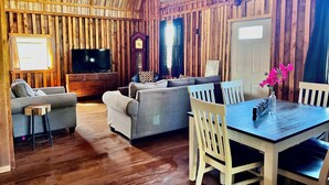 Un interior rústico de madera con sofá, televisor, mesa de comedor y sillas.