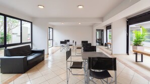 Een ruime binnenruimte met een lange tafel en stoelen, een bank en grote ramen.