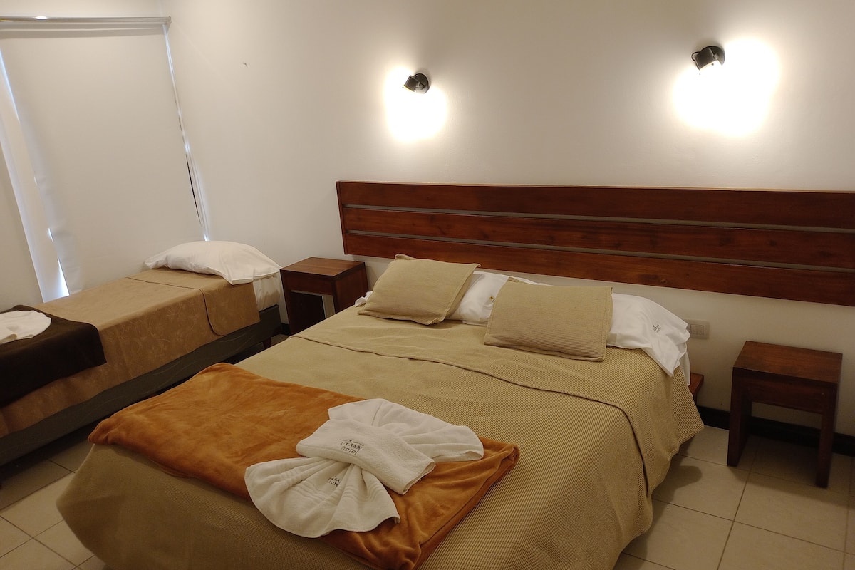 A hotel room with two beds, a wooden headboard, bedside tables, and wall-mounted lights.