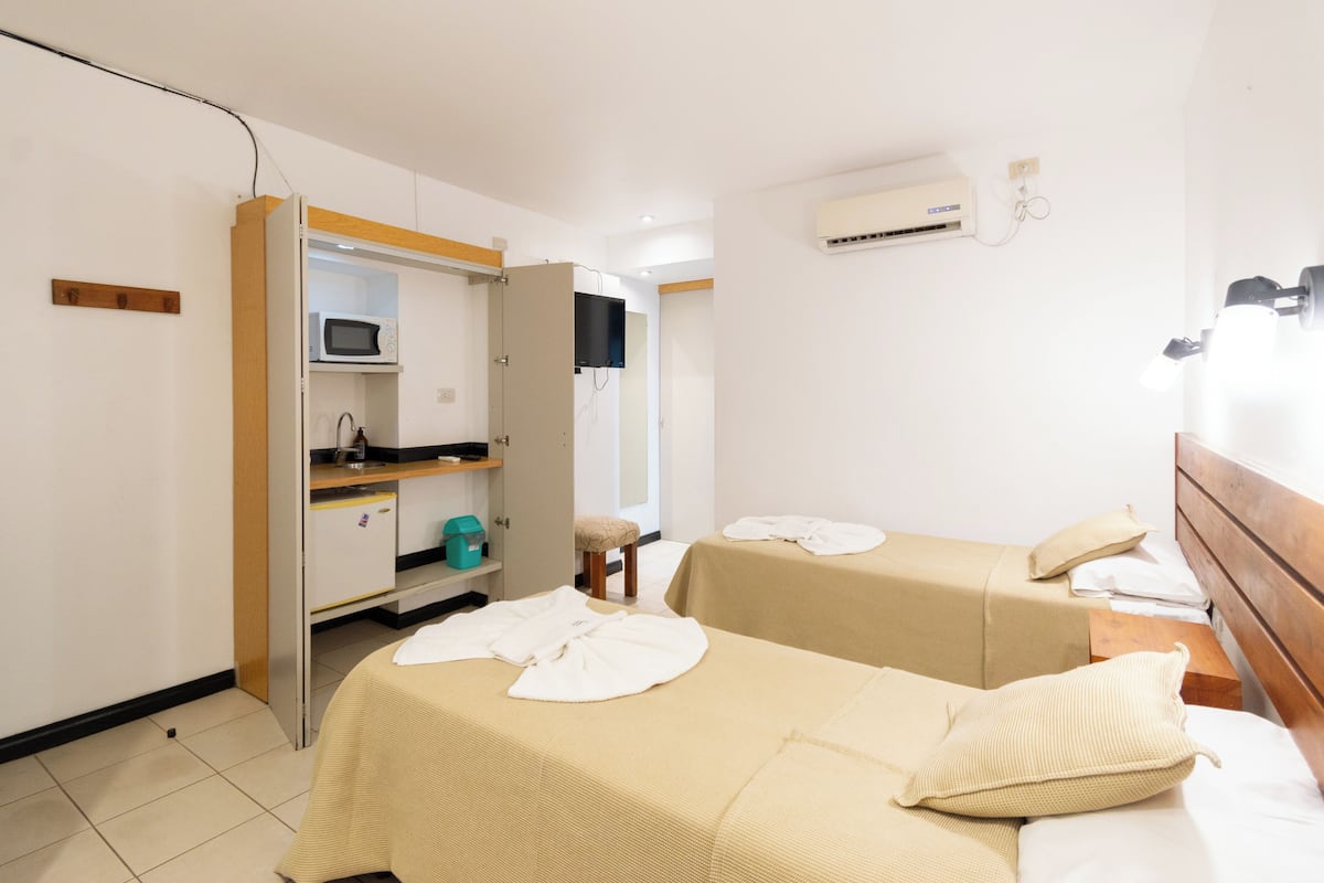 A hotel room with two beds, a microwave, a small kitchenette, and an air conditioning unit.