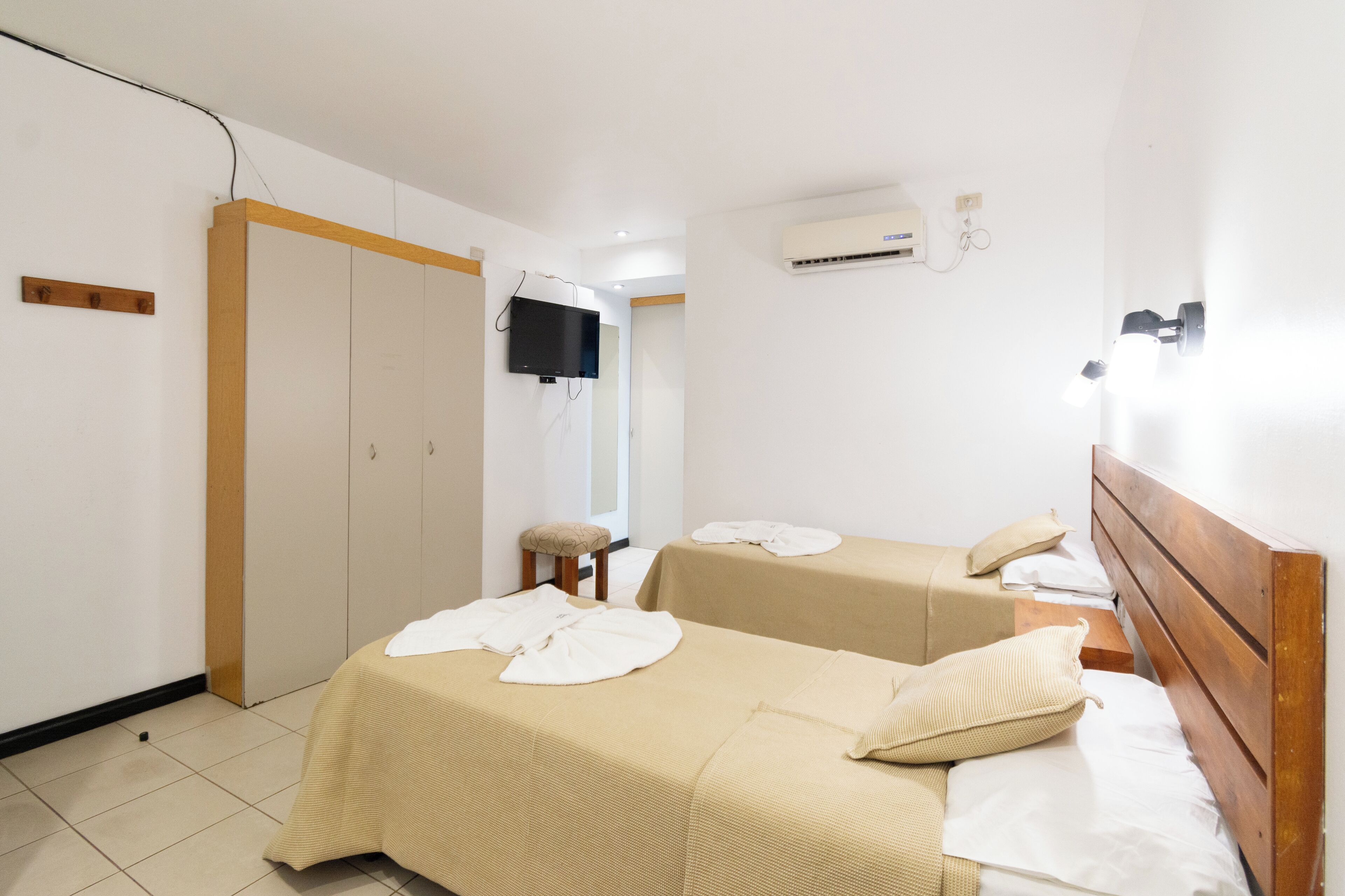Habitación de hotel con dos camas, televisor, aire acondicionado y un taburete pequeño.