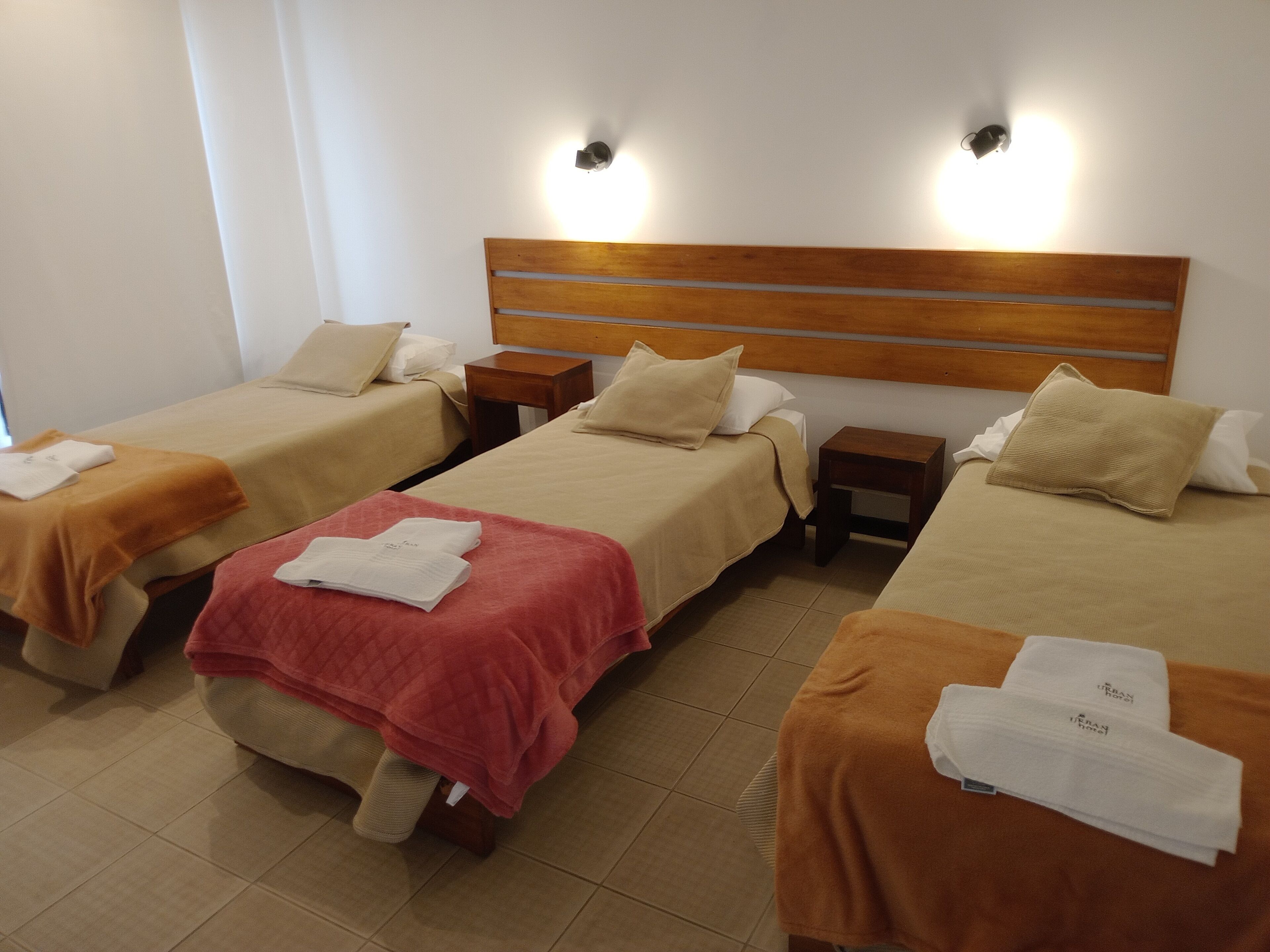 A hotel room with three single beds, each with a wooden headboard, white linens, and a small bedside table.