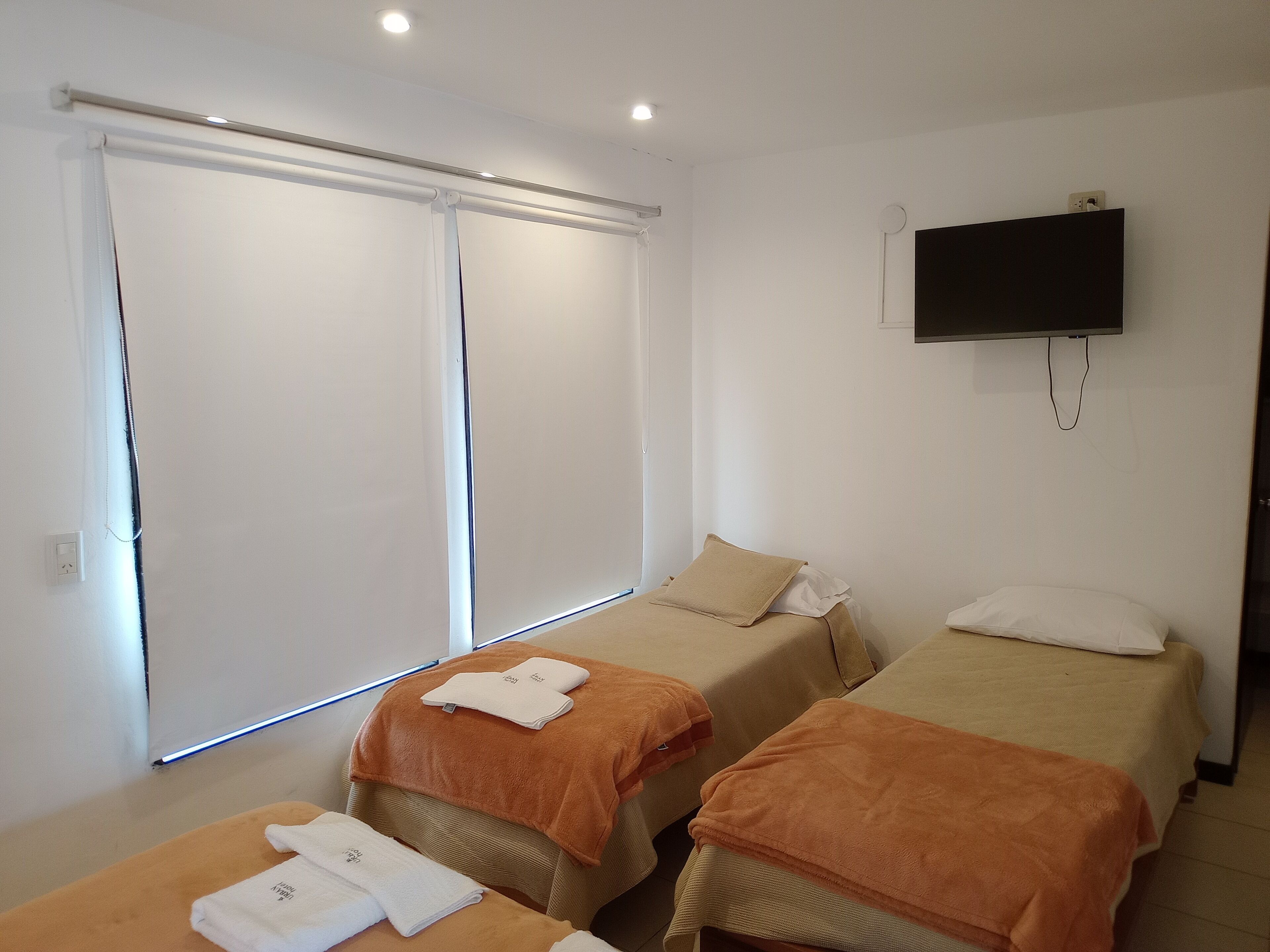 Habitación de hotel con dos camas, un televisor montado en la pared y una ventana con persianas.