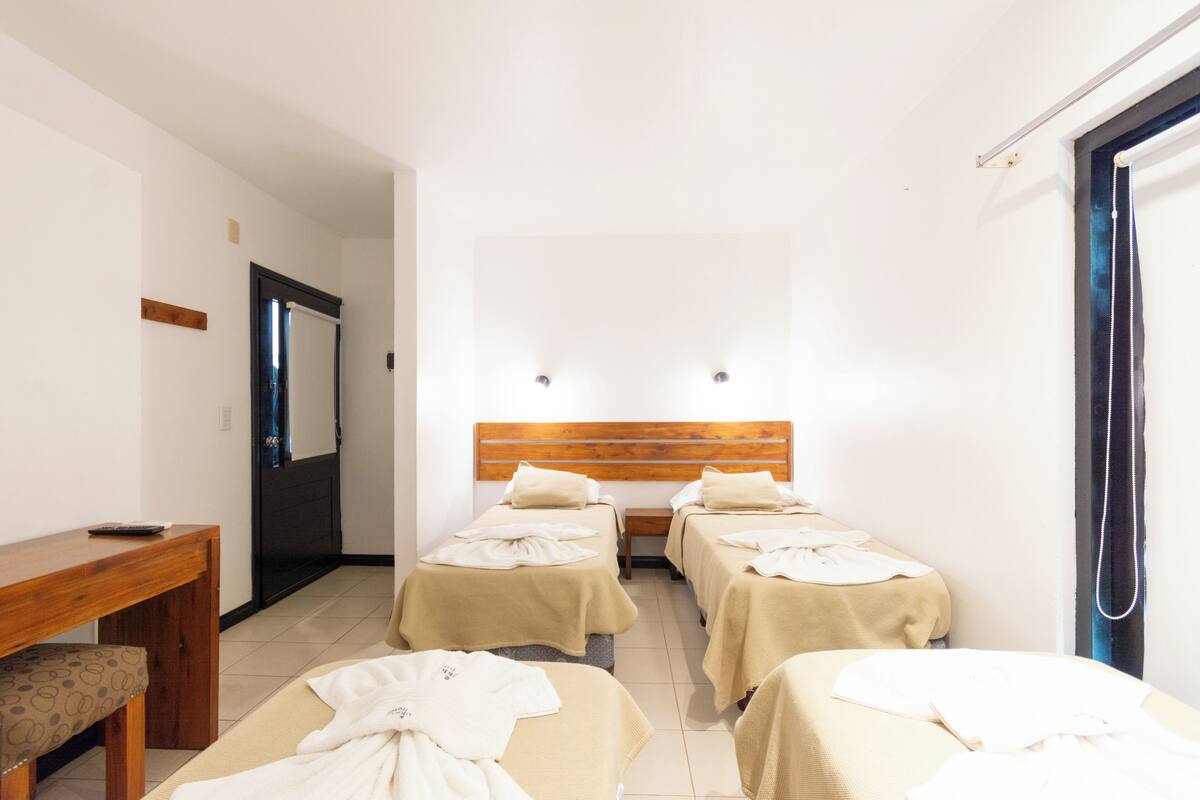 A hotel room with two single beds, a wooden headboard, a small table, and a bench.
